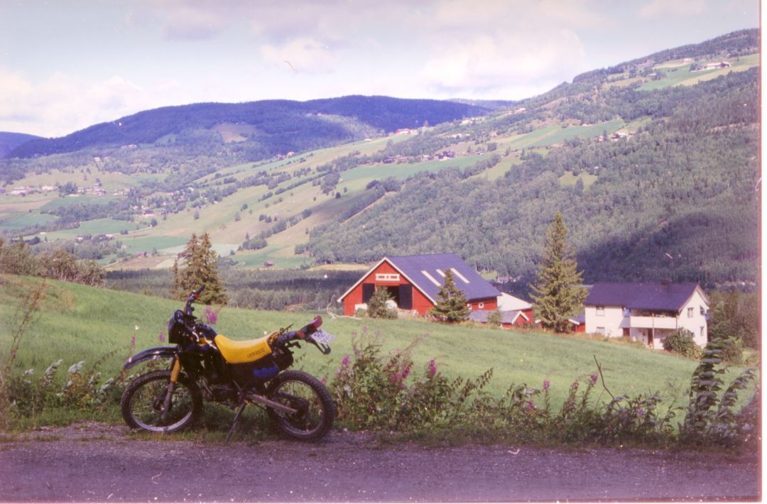 En gul motorsykkel står parkert foran en rød, norsk låve. 